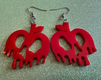 May include: A pair of red, dripping apple earrings with a skull design. The earrings are made of acrylic and have silver hooks.