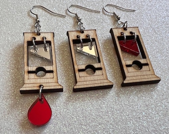 May include: Three pairs of wooden guillotine earrings with a red, silver, and clear glass blade. The earrings are on a white background.