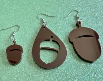 May include: Three pairs of brown acorn earrings. The earrings are made of acrylic and have a shiny finish. The smallest pair is a simple acorn shape, the middle pair is a teardrop shape with an acorn cutout, and the largest pair is a larger acorn shape.
