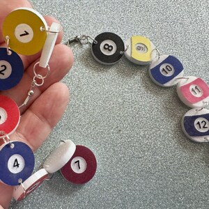 May include: A colorful necklace made of wooden billiard balls with numbers 1 through 13. The balls are connected with silver jump rings.