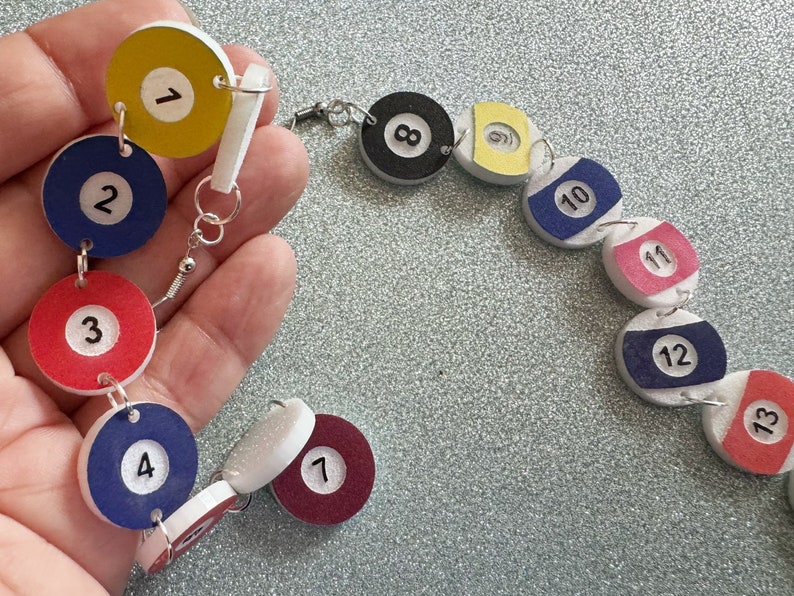 May include: A colorful necklace made of wooden billiard balls with numbers 1 through 13. The balls are connected with silver jump rings.