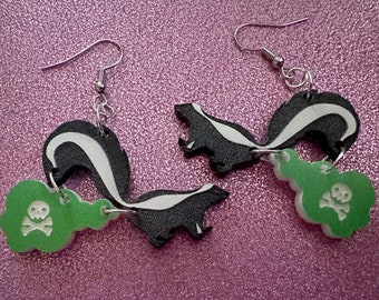 May include: A pair of dangle earrings featuring black and white skunk silhouettes with green skull and crossbones charms.