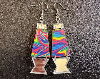 May include: A pair of colorful earrings with a rainbow swirl pattern and a clear, reflective, geometric shape. The earrings are made of acrylic and have silver hooks.