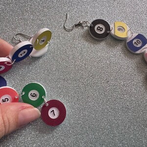 May include: A set of 12 colorful, round, numbered earrings, each with a white background and black numbers. The earrings are connected by silver jump rings and are in the shape of a circle.