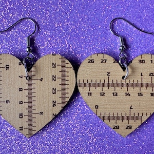 May include: A pair of wooden heart-shaped earrings with a ruler design. The earrings are brown and have silver hooks.