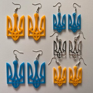 May include: A set of six earrings featuring the Ukrainian trident symbol. The earrings are available in three colors: yellow, blue, and silver.