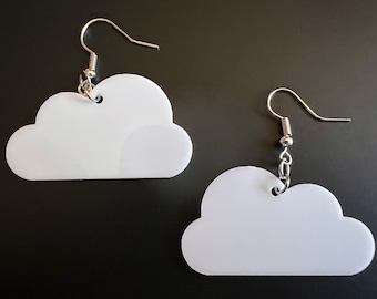 May include: A pair of white cloud-shaped earrings. Each earring features a cloud cutout with a silver-colored fish hook. The earrings are hanging against a dark background. The earrings are a fun and whimsical accessory.