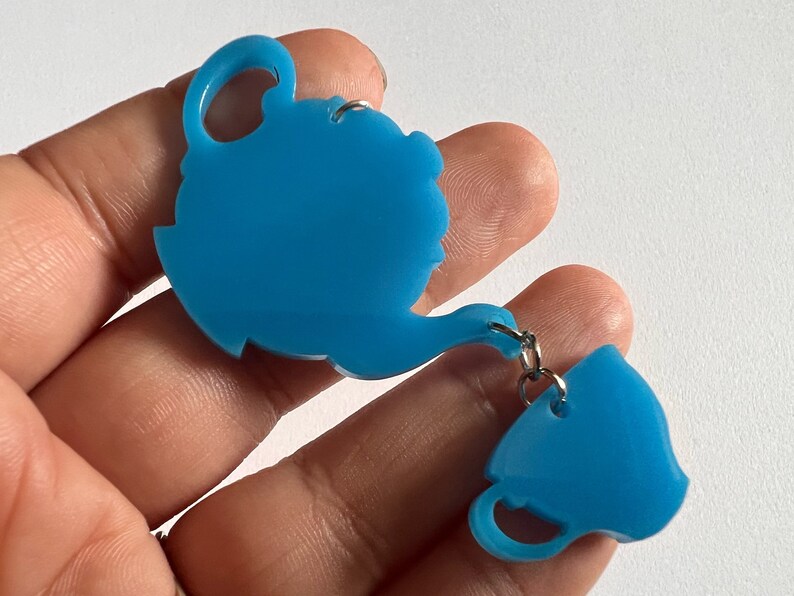 May include: A teal blue teapot and teacup charm with a silver chain connecting them.