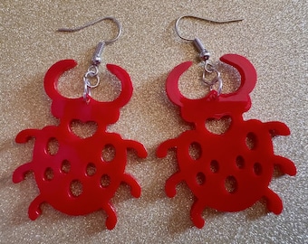 May include: A pair of red ladybug earrings with silver hooks. The earrings are made of acrylic and have a shiny finish.