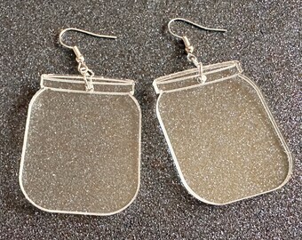 May include: A pair of clear acrylic earrings shaped like mason jars. The earrings have silver hooks.