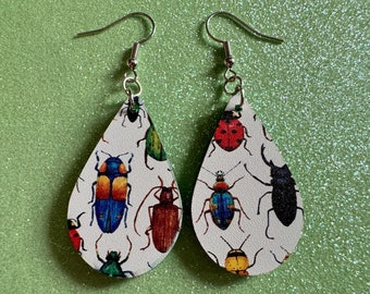 May include: A pair of teardrop-shaped earrings with a white background and a colorful insect pattern. The earrings are made of metal and have a silver finish.