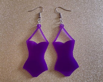 May include: A pair of purple earrings shaped like a swimsuit. The earrings have silver hooks.