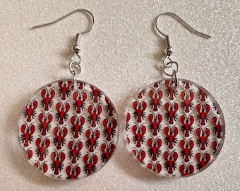 May include: A pair of round, clear acrylic earrings with a lobster pattern. The earrings have silver hooks.