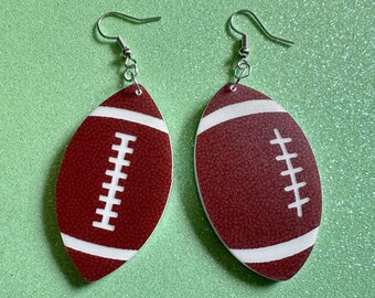 May include: A pair of brown and white football-shaped earrings with silver hooks. The footballs have white stitching details.