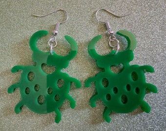 May include: A pair of green ladybug earrings with silver hooks. The earrings are made of acrylic and have a cutout design.