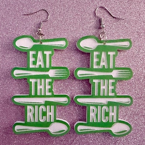 May include: A pair of green earrings with a white design. The earrings feature a spoon, fork, and knife with the text "Eat the Rich" on each earring.