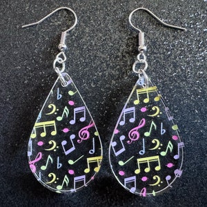 May include: A pair of teardrop-shaped earrings with silver hooks. The earrings are made of clear acrylic and feature a colorful pattern of musical notes and dots.