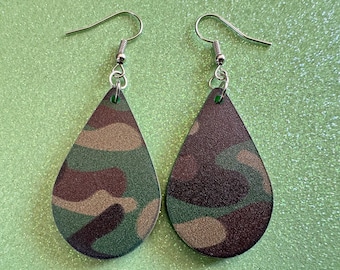 May include: A pair of teardrop-shaped earrings with a camouflage pattern in shades of green, brown, and tan. The earrings have silver hooks.