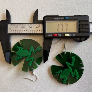 May include: Green frog earrings with a lily pad design. The earrings are 1.77 inches in diameter.
