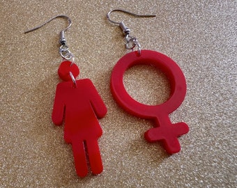 May include: A pair of earrings with red, gender symbol charms. One earring features a female symbol and the other a stylized human figure.