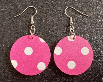 May include: A pair of pink and white polka dot earrings with silver hooks. The earrings are round and have a textured surface.