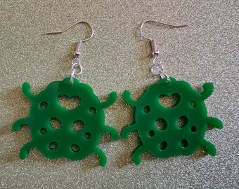 May include: A pair of green ladybug earrings with a heart cutout and silver hooks.