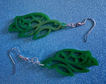May include: A pair of green turtle-shaped earrings with silver hooks. The turtles are detailed with a patterned shell and have a delicate, intricate design.