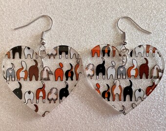 May include: A pair of heart-shaped earrings with a clear background and a pattern of colorful dog butts. The earrings have silver hooks.