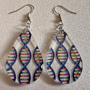 Peut inclure: Une paire de boucles d'oreilles en forme de goutte avec un crochet argenté et un fond transparent. Les boucles d'oreilles présentent un motif d'hélice double d'ADN coloré.