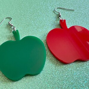 May include: A pair of dangle earrings shaped like apples. One earring is green and the other is red.