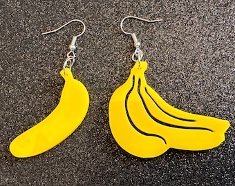 May include: A pair of yellow banana-shaped earrings with silver hooks. The earrings are made of acrylic and are about 2 inches long.