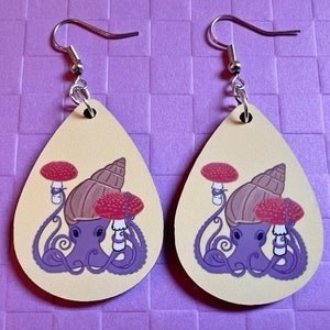 May include: Two teardrop-shaped earrings with a light yellow background. Each earring features a purple octopus with a brown snail shell on its head. The octopus is holding two red and white mushrooms. The earrings have silver hooks.