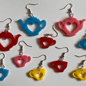 May include: Nine pairs of earrings featuring teapots and teacups with heart cutouts. The earrings are made of acrylic and come in blue, red, and yellow.