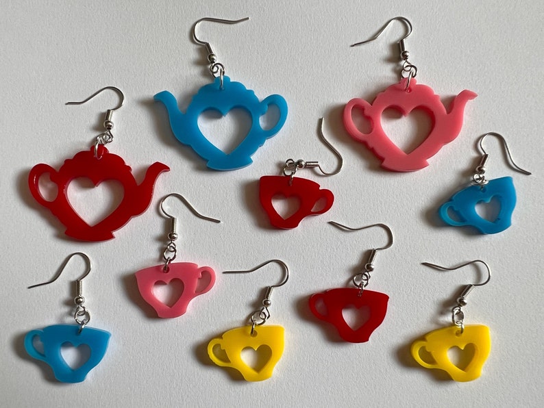 May include: Nine pairs of earrings featuring teapots and teacups with heart cutouts. The earrings are made of acrylic and come in blue, red, and yellow.