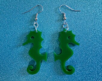 May include: A pair of green seahorse earrings with silver hooks. The seahorses are made of a smooth, shiny material.