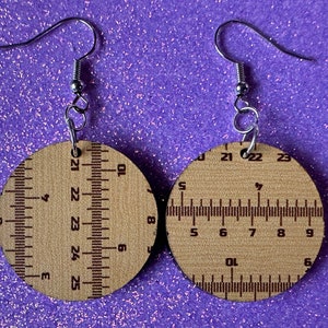 May include: A pair of wooden earrings with a ruler design. The earrings are brown with black markings and have silver hooks.