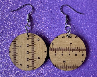 May include: A pair of wooden earrings with a ruler design. The earrings are brown with black markings and have silver hooks.