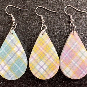 May include: Three pairs of teardrop-shaped earrings with a plaid pattern in shades of yellow, pink, and blue. The earrings have silver hooks.
