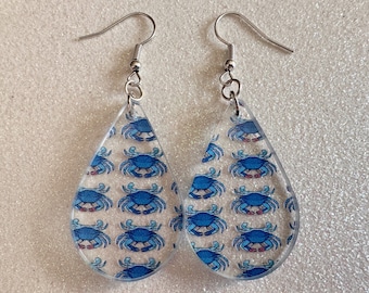 May include: A pair of teardrop-shaped earrings with a blue crab pattern. The earrings are made of clear acrylic and have silver hooks.