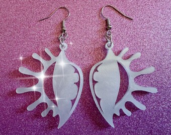 May include: A pair of white acrylic earrings shaped like an eye with a sunburst design. The earrings have silver hooks.
