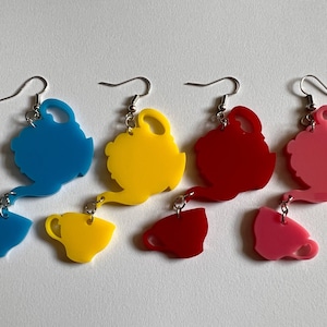 May include: Four pairs of dangle earrings featuring a teapot and teacup design. The teapots are blue, yellow, red, and pink. The teacups are the same colors as the teapots.