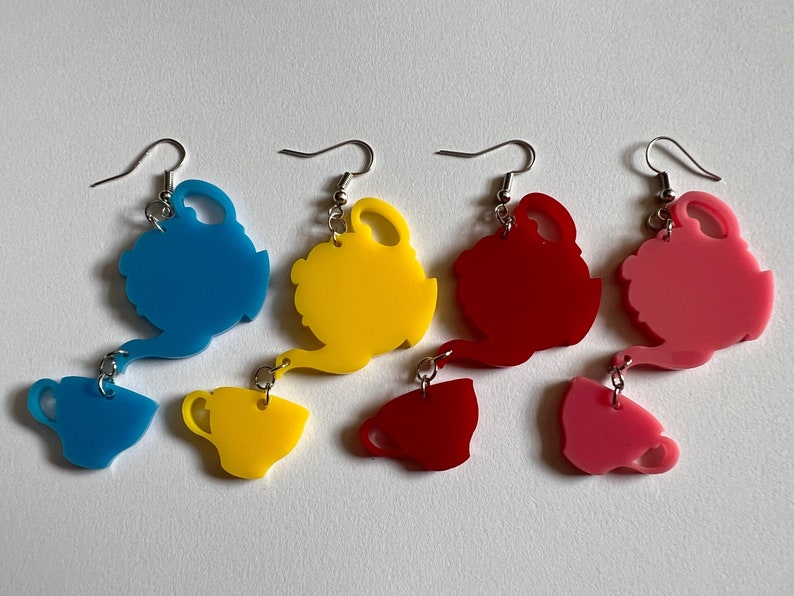 May include: Four pairs of dangle earrings featuring a teapot and teacup design. The teapots are blue, yellow, red, and pink. The teacups are the same colors as the teapots.