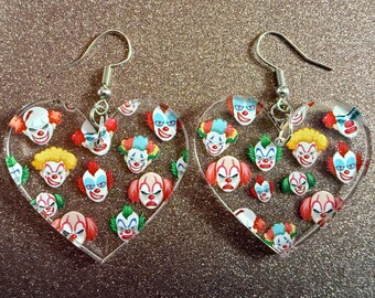 May include: A pair of heart-shaped earrings with a silver tone finish. Each earring features a clear background with a pattern of colorful clown faces.