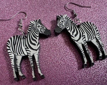 May include: A pair of black and white zebra earrings with silver hooks. The zebras are made of wood and have a detailed design.