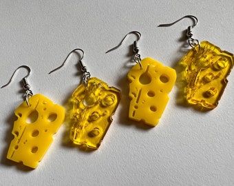 May include: Four pairs of earrings featuring yellow cheese-shaped charms with holes. The earrings have silver hooks.