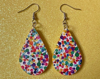 May include: A pair of teardrop-shaped earrings with a white background and a colorful confetti pattern. The earrings are made of leather and have silver hooks.