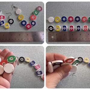 May include: A pair of earrings made from white plastic circles with numbers 1 through 15 printed on them, resembling billiard balls. The earrings are connected by silver jump rings. The earrings are shown on a ruler, measuring approximately 6 inches in length.