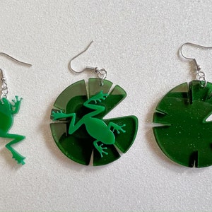 May include: Three pairs of green acrylic earrings. One pair features a frog silhouette, while the other two pairs feature a lily pad design.