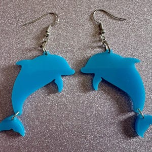 May include: A pair of blue dolphin earrings with silver hooks. The dolphins are facing opposite directions and have a shiny finish.