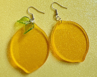 May include: A pair of yellow lemon-shaped earrings with green glitter leaves. The earrings are made of resin and have silver hooks.
